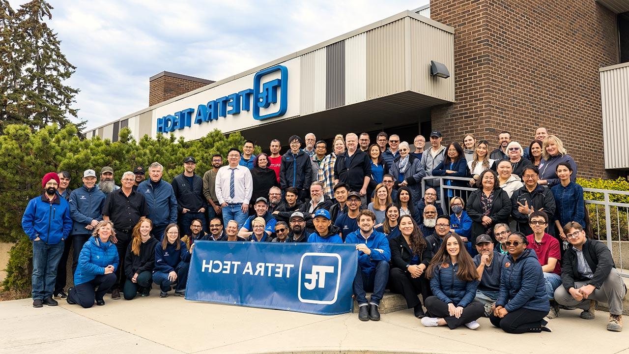 Large group of Tetra Tech employees in front of an office building holding Tetra Tech signage